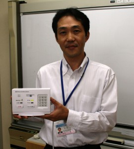安否確認の独自センサー内蔵システムを手にする尾崎常務